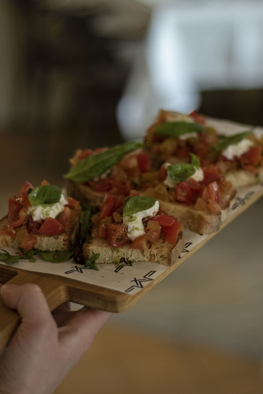 Bruschetta met cherrytomaatjes, basilicum en burrata op een houten plank bij Maximiliano