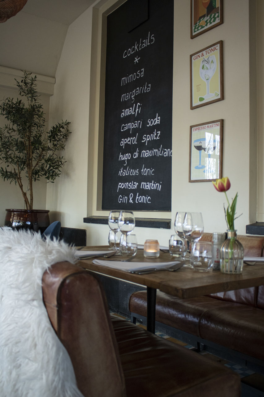 Een gedekte tafel bij Maximiliano met leren stoelen en een krijtbord vol aperitivi